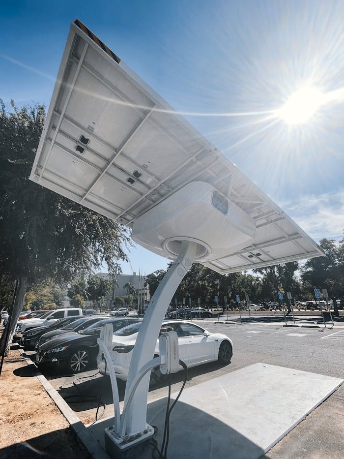 Electric car charging station equipped with solar panels in a sunny parking lot.